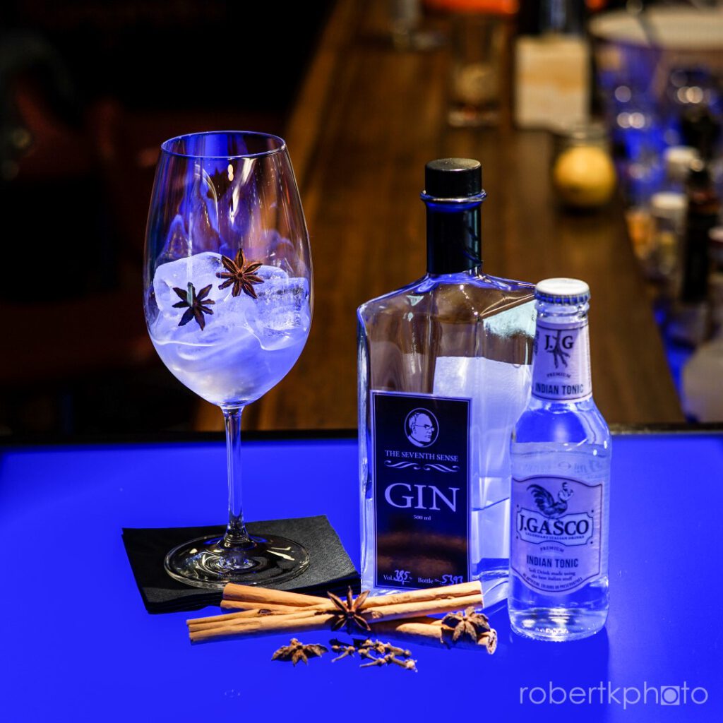 Gin bottles with a blue-lit glass of gin garnished with spices at a bar