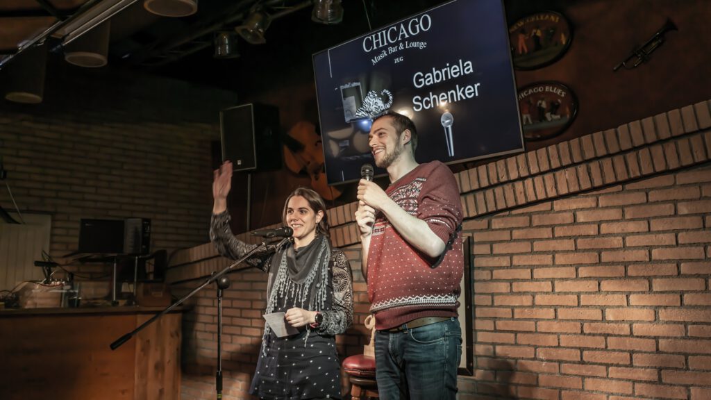 Two Poetry Slam performers standing together beneath the event screen