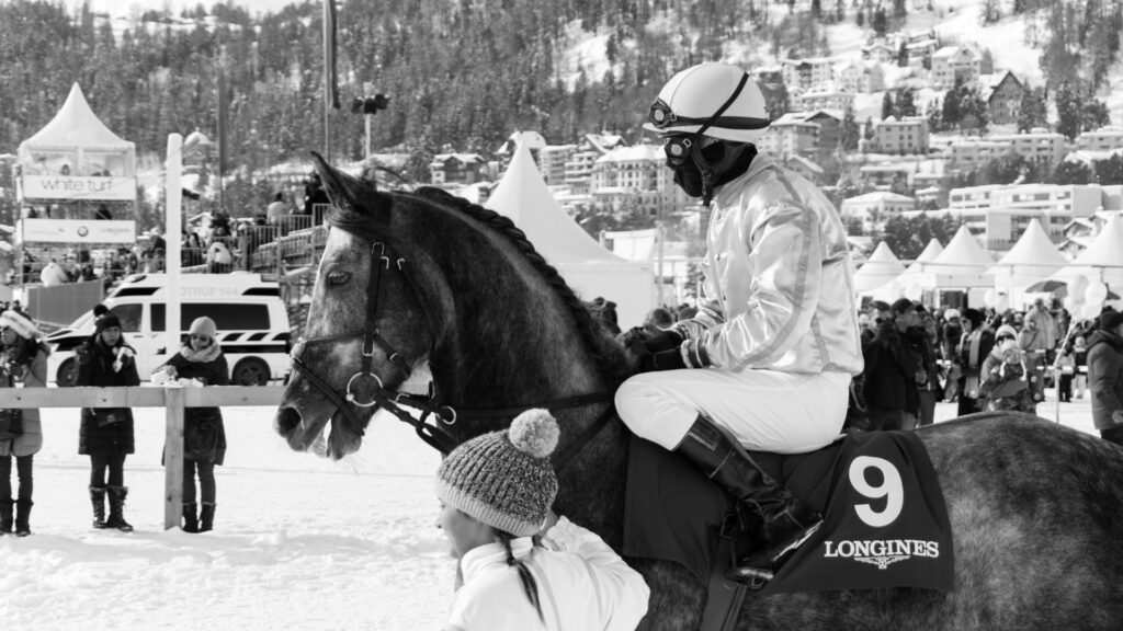 Jockey in white racing silks beside horse number 9 at White Turf St. Moritz
