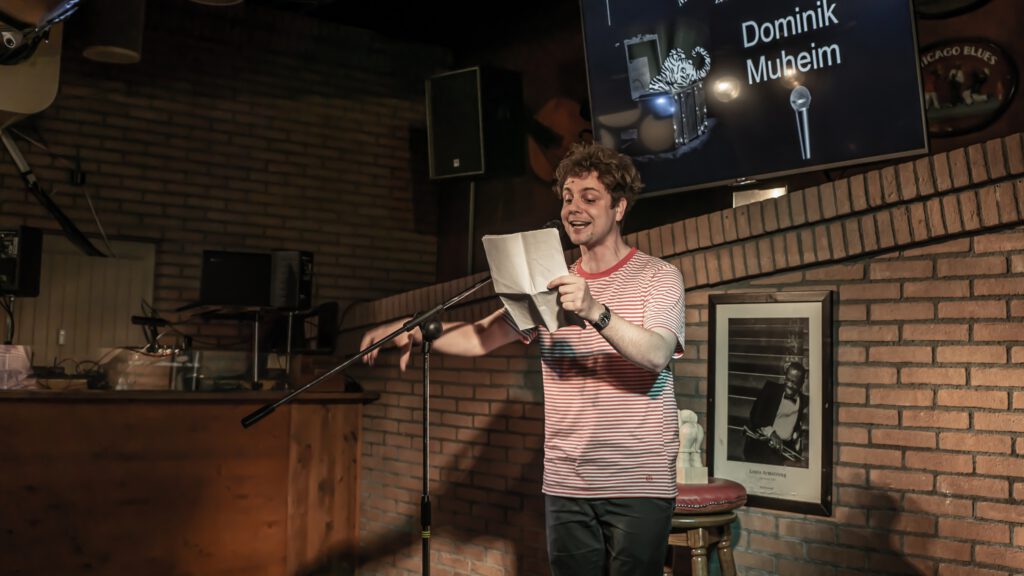 Man in a striped shirt reading from papers at the Poetry Slam microphone