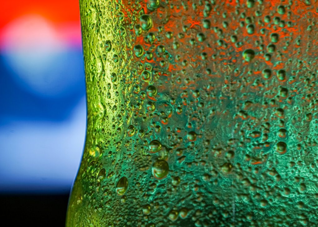 Close-up of a green glass bottle with a blurred colorful background