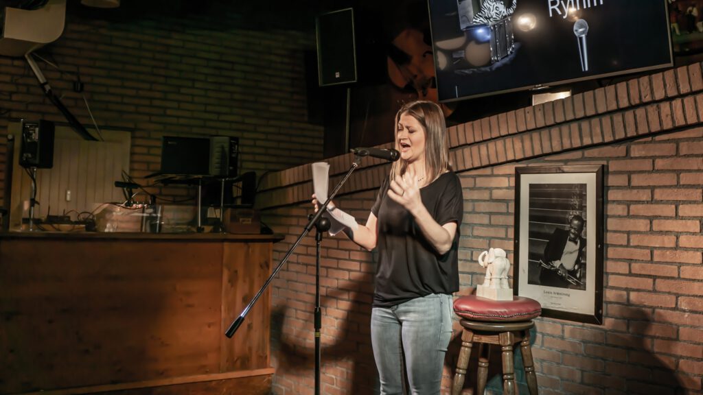 Woman in a black shirt reading and gesturing at the Poetry Slam microphone