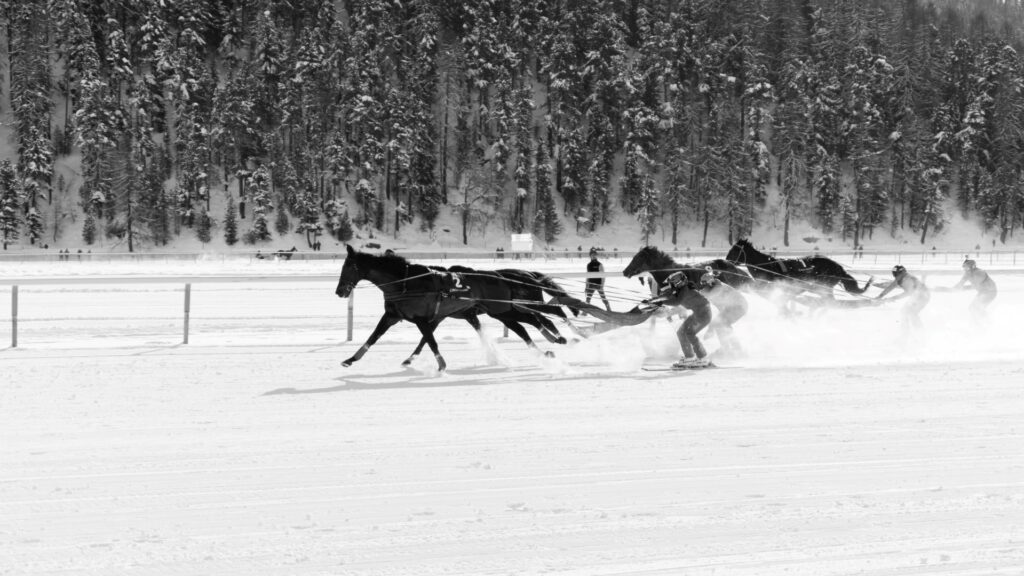 Side view of horses and skiers racing through snow at White Turf