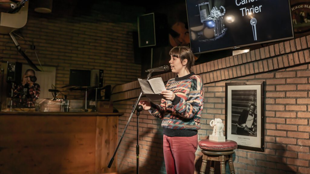 Woman in a patterned sweater reading from papers at the microphone