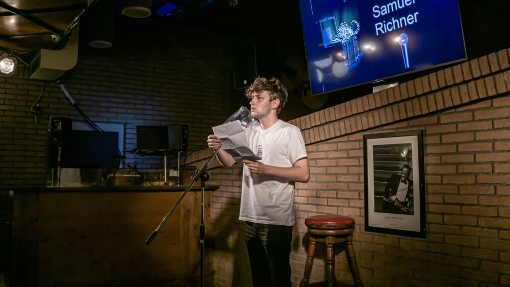 Young male performer reading from papers at the Poetry Slam microphone