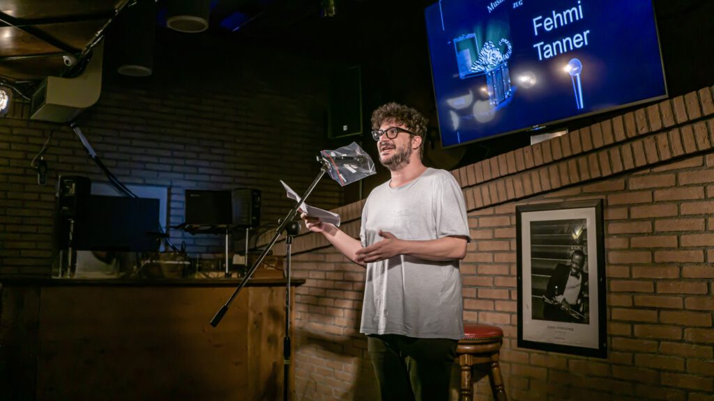 Man in glasses reading from a booklet at the Poetry Slam microphone