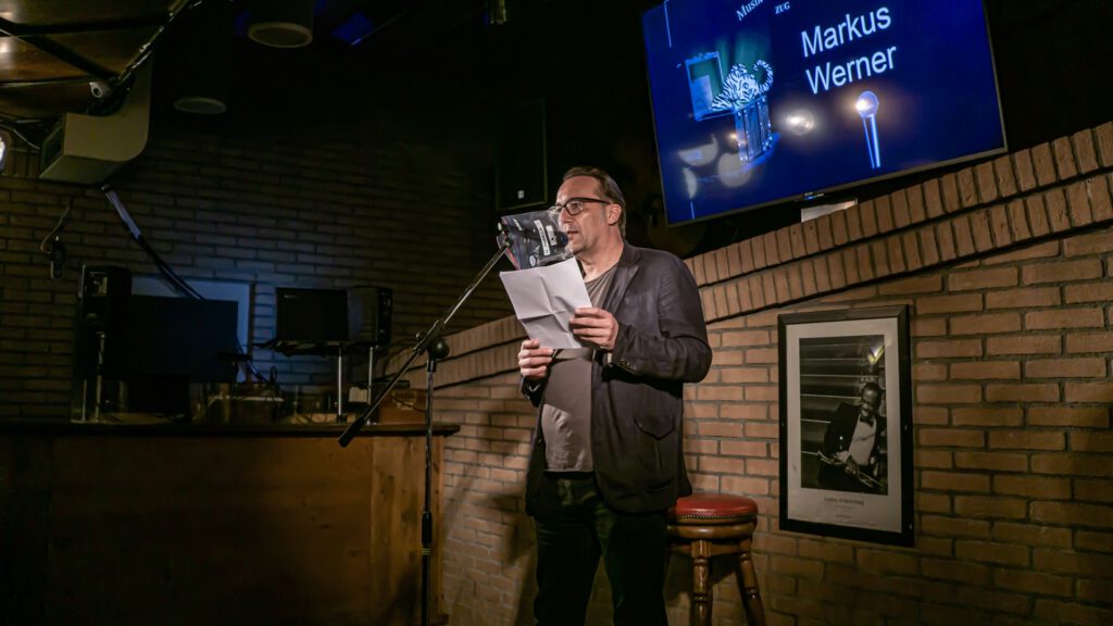 Man in a jacket reading from papers at the Poetry Slam microphone