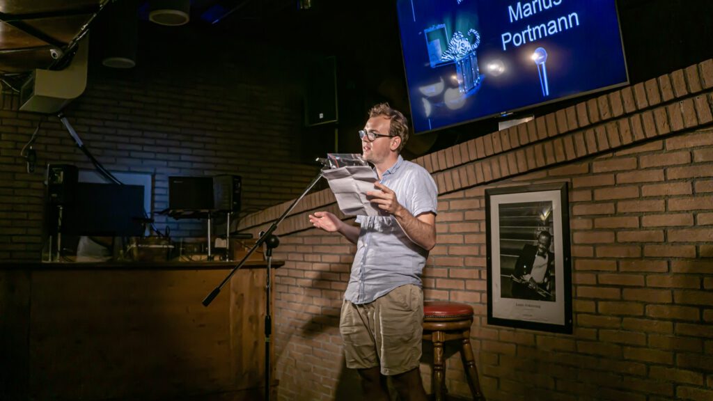 Wide view of a Poetry Slam performer reading beneath the event screen