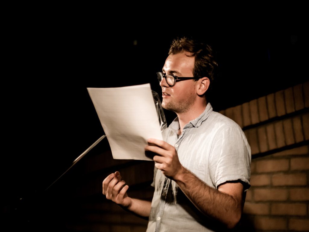 Man in glasses reading from a large sheet of paper on stage