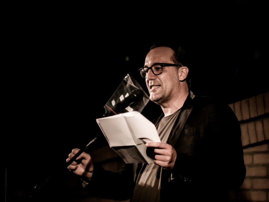 Man in glasses reading from papers at a Poetry Slam microphone
