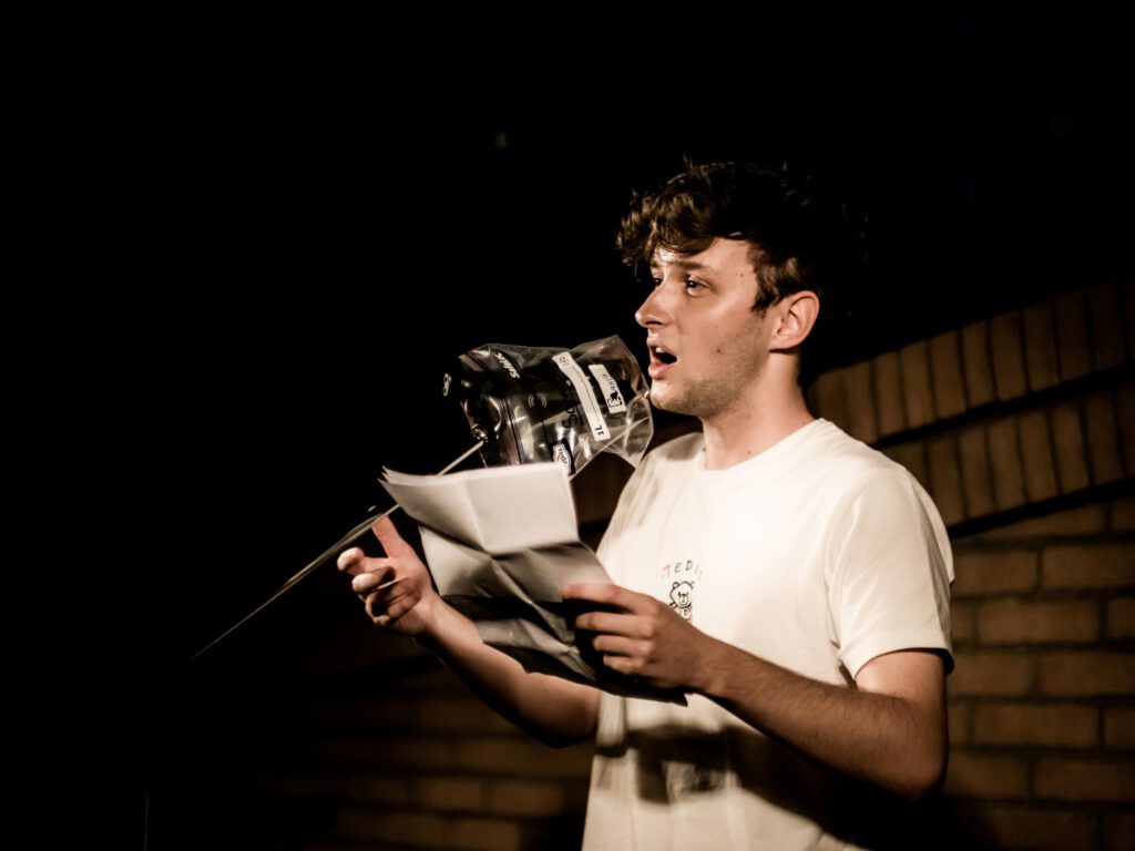 Young male performer reading from papers at a Poetry Slam microphone